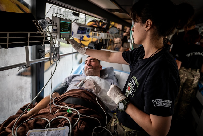 A woman looks at medical equipment hanging over a patient's bed on a bus