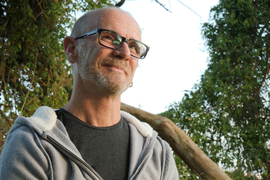A man with glasses looking away with trees and sky behind him