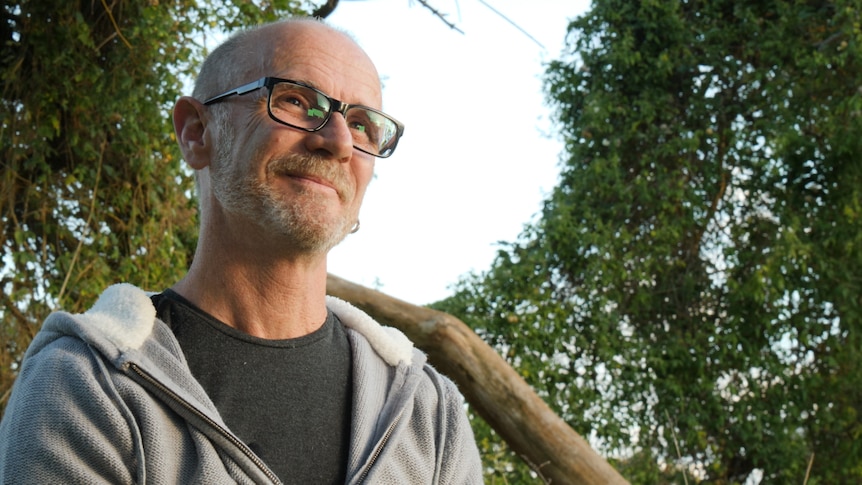 A man with glasses looking away with trees and sky behind him