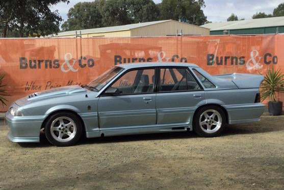 A boxy 1988 VL Walkinshaw Commodore in Panorama Silver parked at an auction lot.