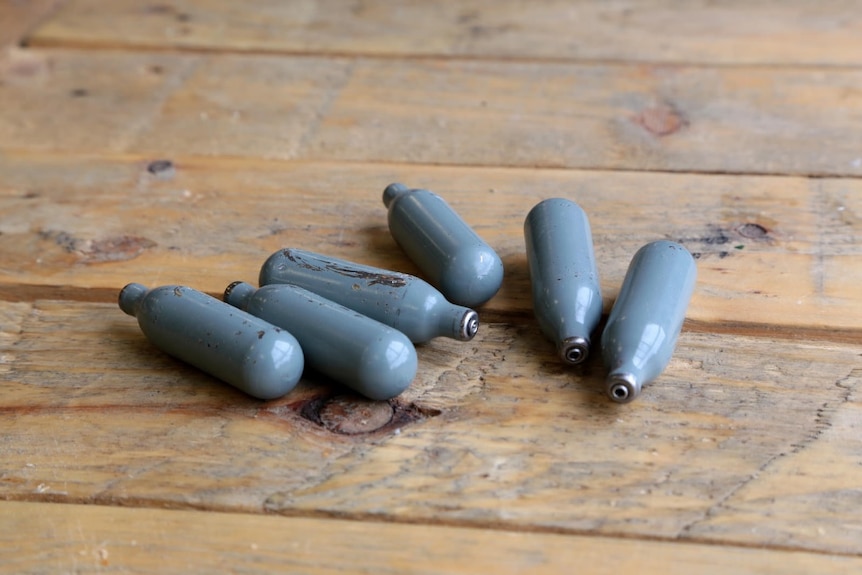 Six small silver bottles on a wooden table.