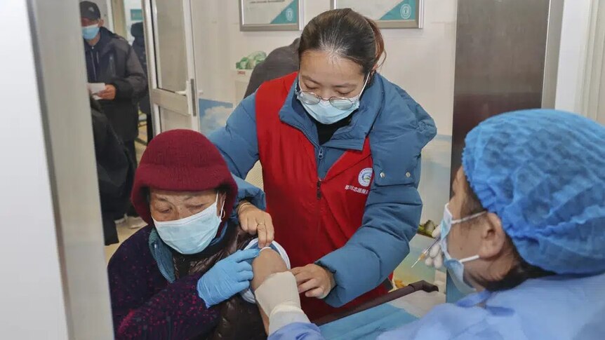 Elderly people roll up their sleeves to be vaccinated by nurses standing around them