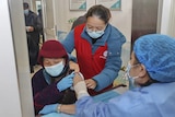 Elderly people roll up their sleeves to be vaccinated by nurses standing around them