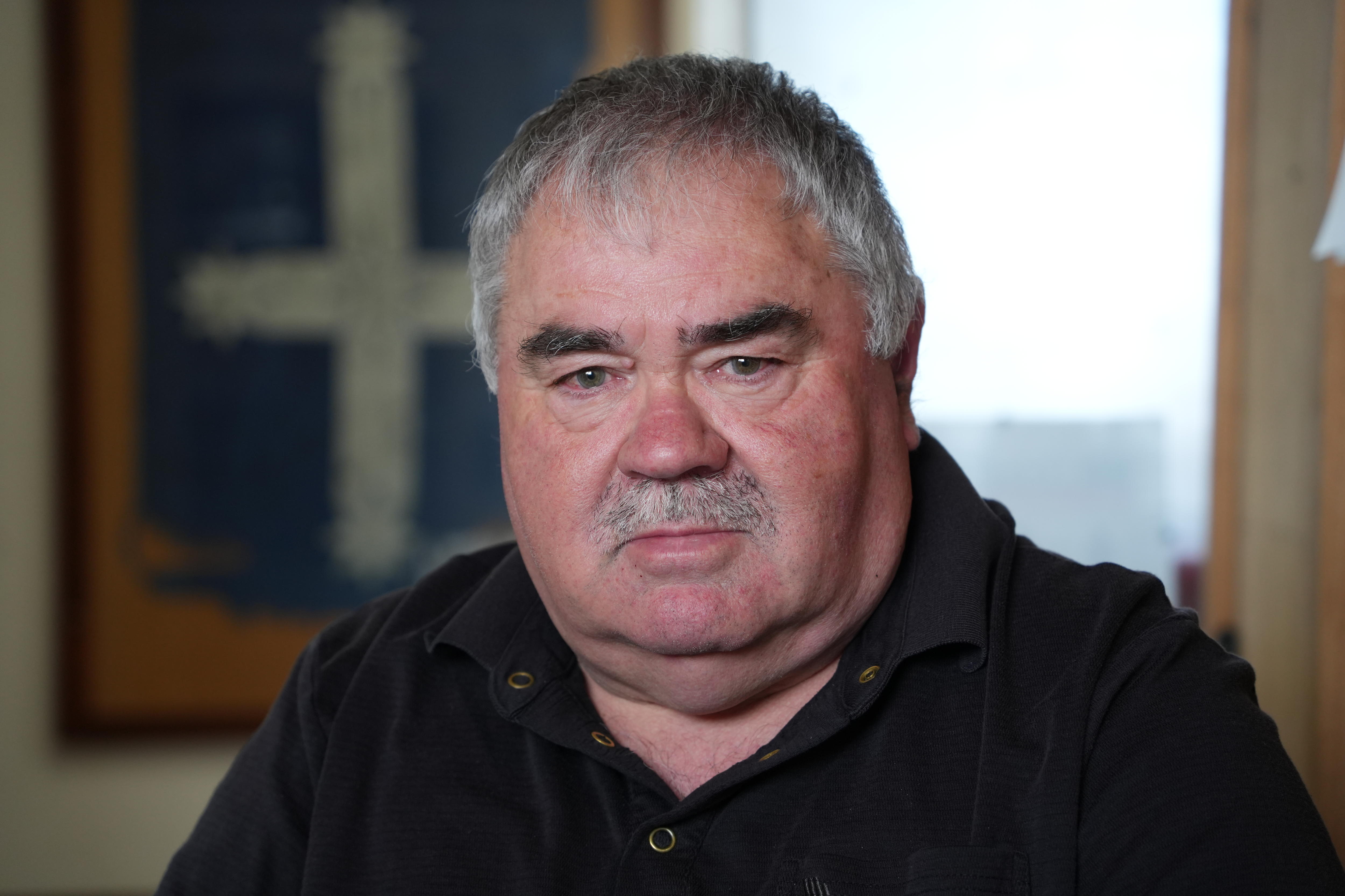 A man (Henry Fuller) with grey hair and grey moustache and full face, wearing a black polo shirt.