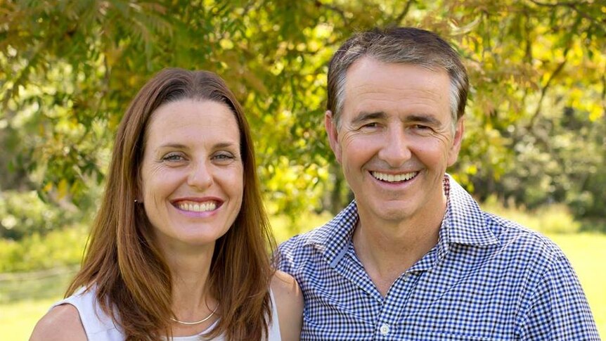 Gerard Rennick, right, next to unnamed woman, left. He wears a checked shirt and smiles with trees behind them.