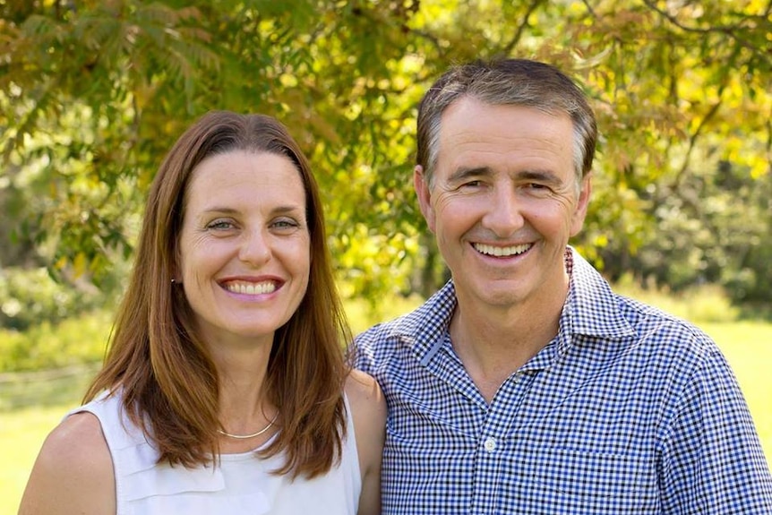 Gerard Rennick, right, next to unnamed woman, left. He wears a checked shirt and smiles with trees behind them.