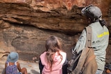 two children and an adult gather round a sandstone cliff with rock art