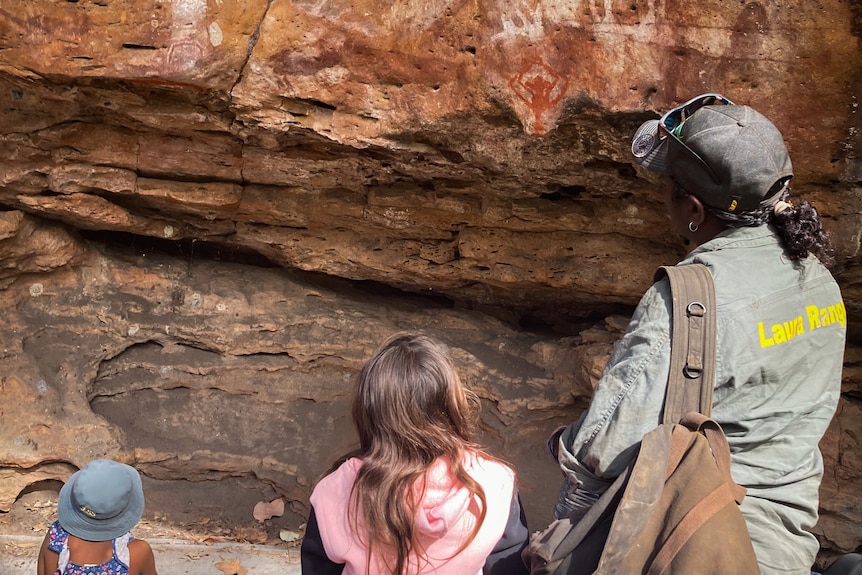 Two children and an adult gather around a sandstone rock with rock art