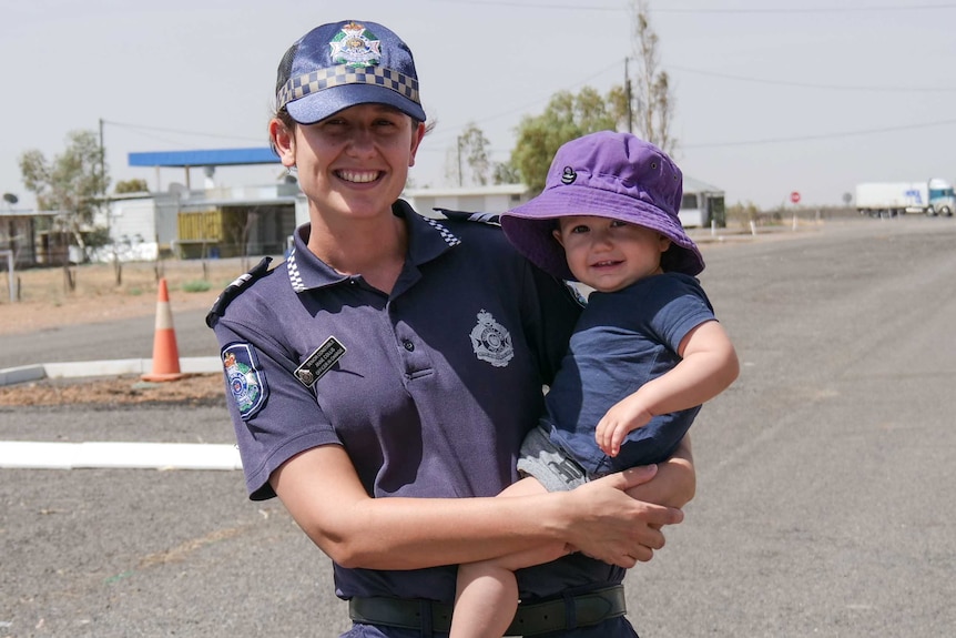 A female police officer stands in an empty street in rural Queensland holding her young son.