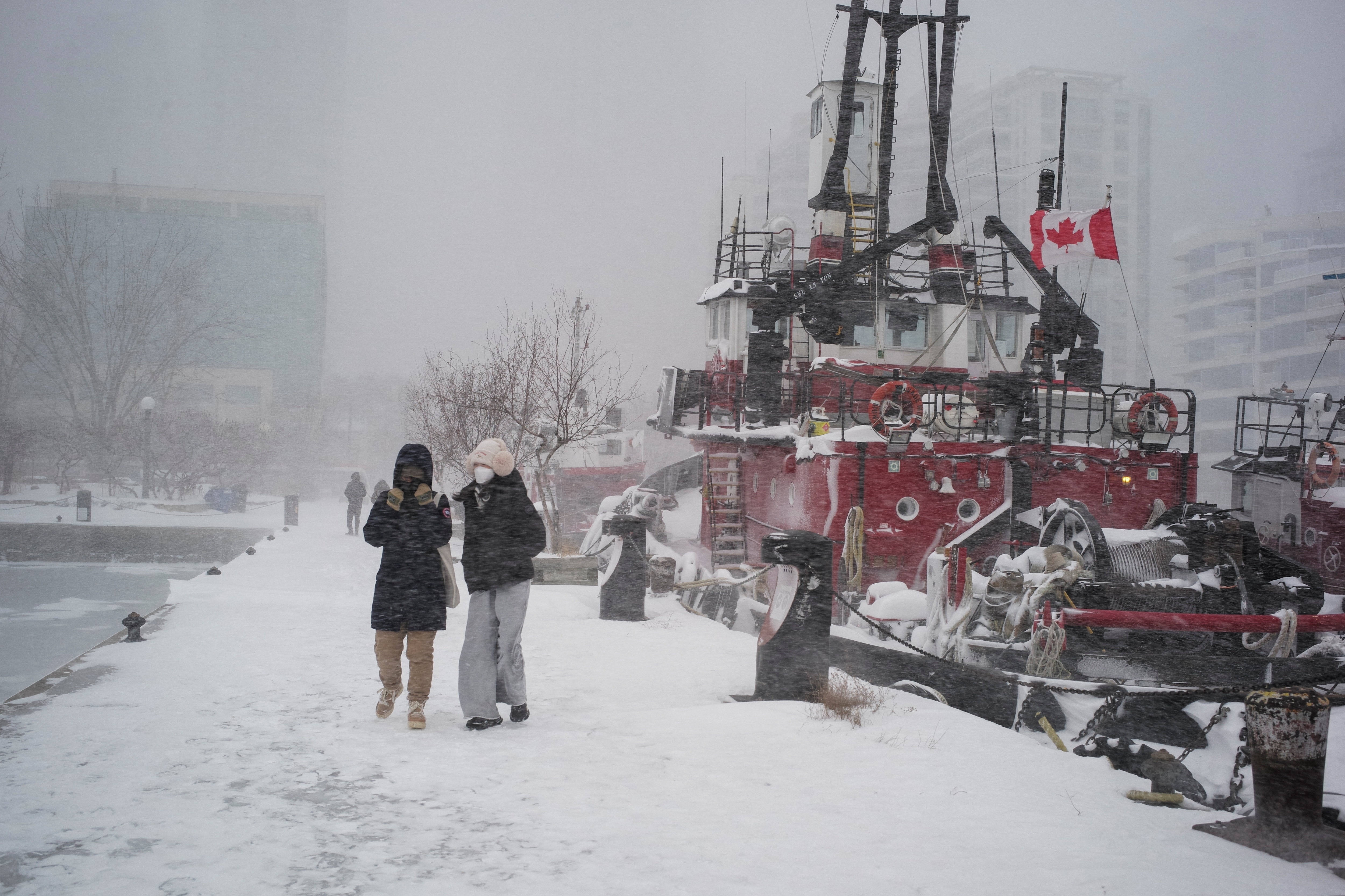 La gente camina junto a un barco cubierto de nieve con una bandera canadiense y un lago.
