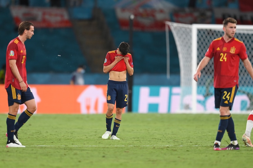 Three dejected Spanish players stand - the one in the middle covering his face  after a draw against Poland at Euro 2020. 
