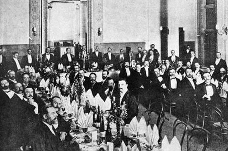A lot of white men in suits sitting at long banquet tables circa 1901