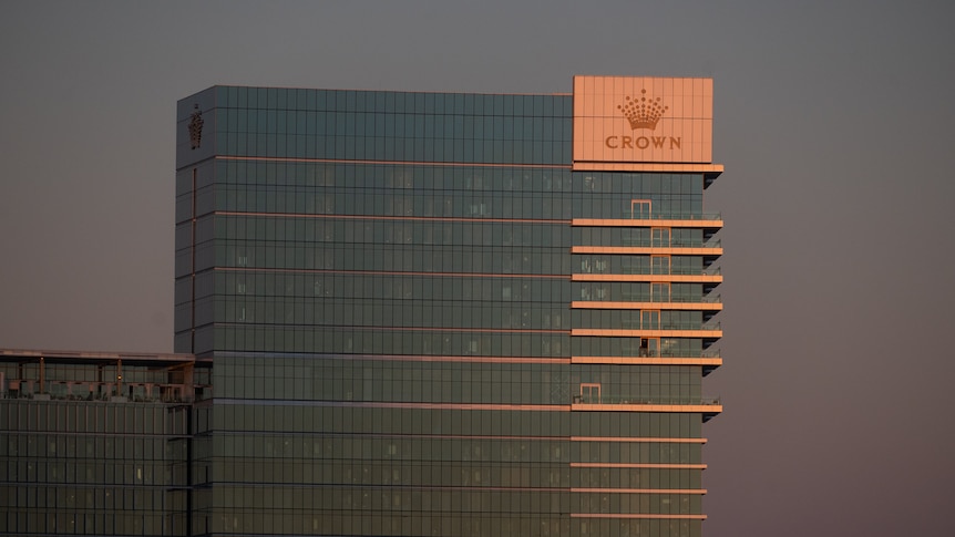 Tall building with Crown logo on the banks of a river in the dusk light.