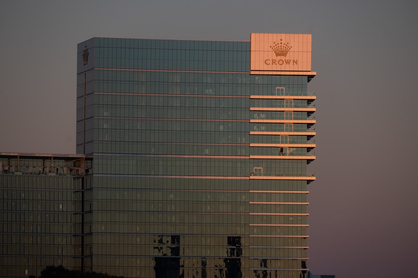 Tall building with Crown logo on the banks of a river in the dusk light.