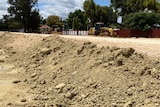 a rising levee made of compacted dirt with a caravan park and machinery in the background
