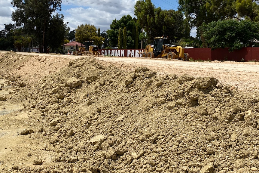 a rising levee made of compacted dirt with a caravan park and machinery in the background