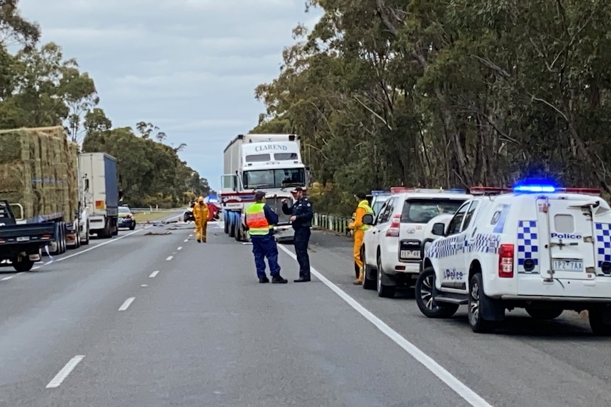 Farm trucks and emergency vehicles line a highway near a fatal crash site.