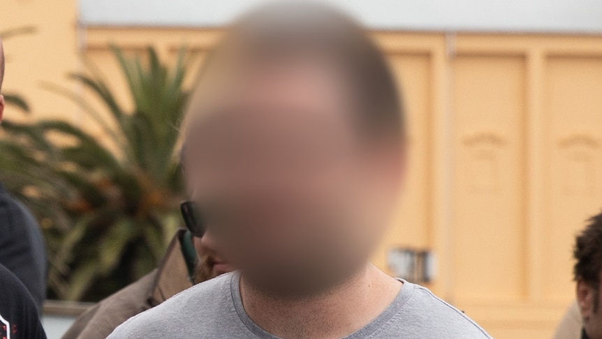 Thomas Sewell, in a grey shirt with his face blurred, walks past fellow members of a neo-Nazi group in Melbourne.