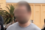 Thomas Sewell, in a grey shirt with his face blurred, walks past fellow members of a neo-Nazi group in Melbourne.