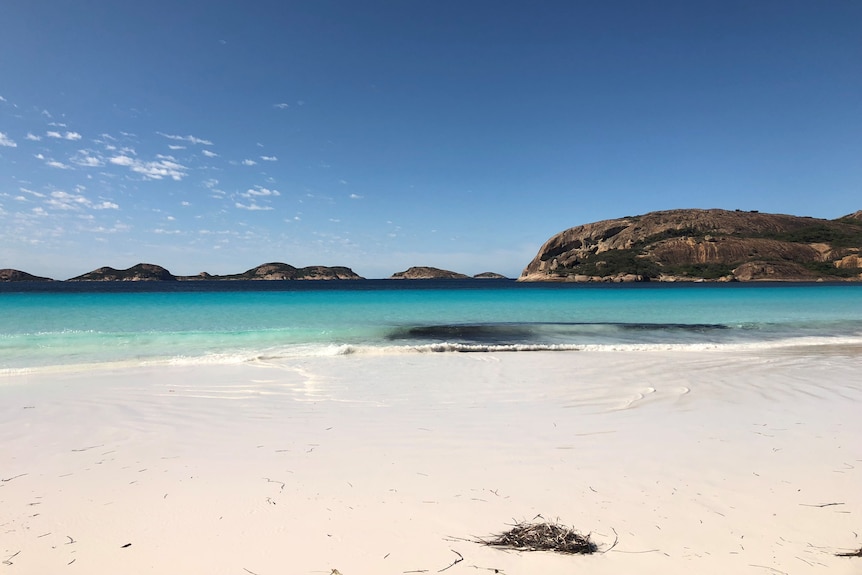 Empty beach with clean white sand and clear water, rocky island in the sea in the background. 