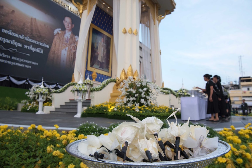 Thai mourners lay down sandalwood flowers in front of a giant portrait of late Thai King Bhumibol.