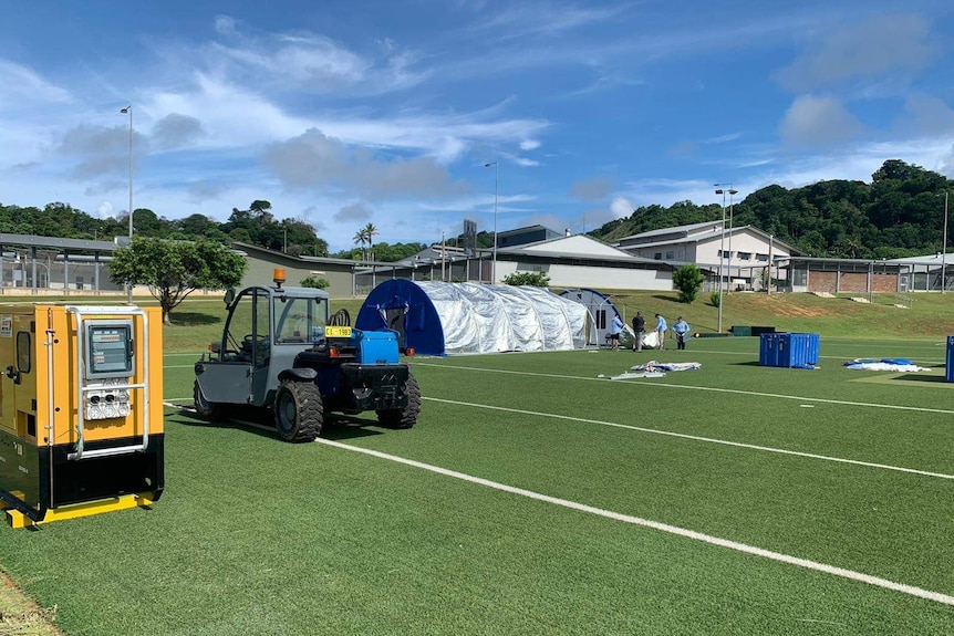 Tents and vehicles are seen in a green field.