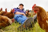Farmer Liam Brokensha smiles for a photo as he lies in a paddock surrounded by chickens.