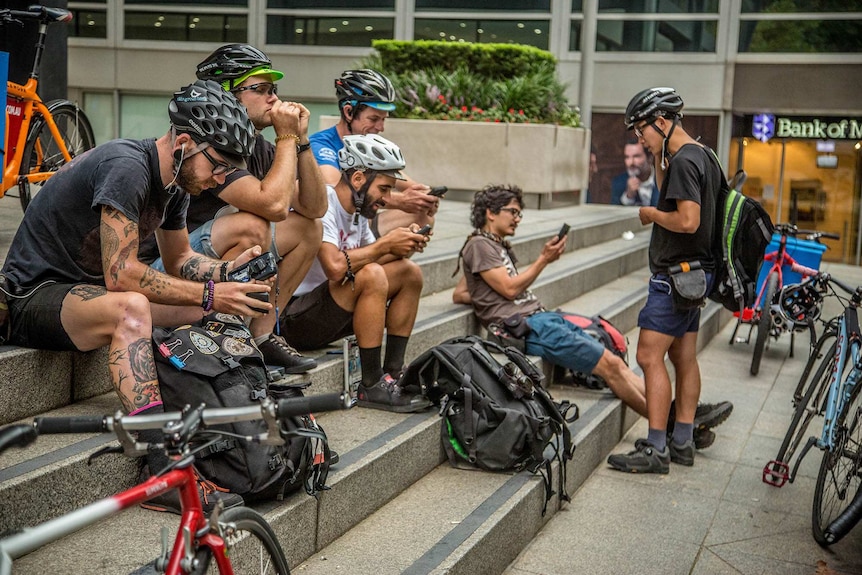 A large group of bike couriers gather on a building's front steps