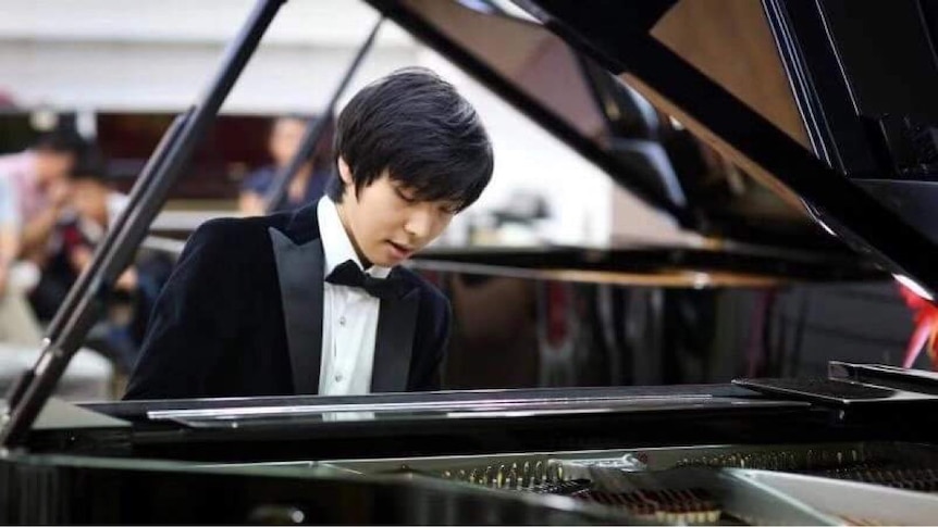 Man wearing tuxedo and playing grand piano. 