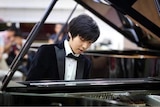 Man wearing tuxedo and playing grand piano. 