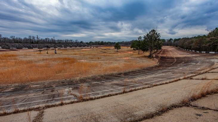 Old tarmac tracks stand out from the long yellow grass at an abandoned speedway track