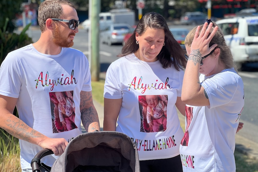 A man and two women, all in matching T-shirts, standing near a road on a sunny day.