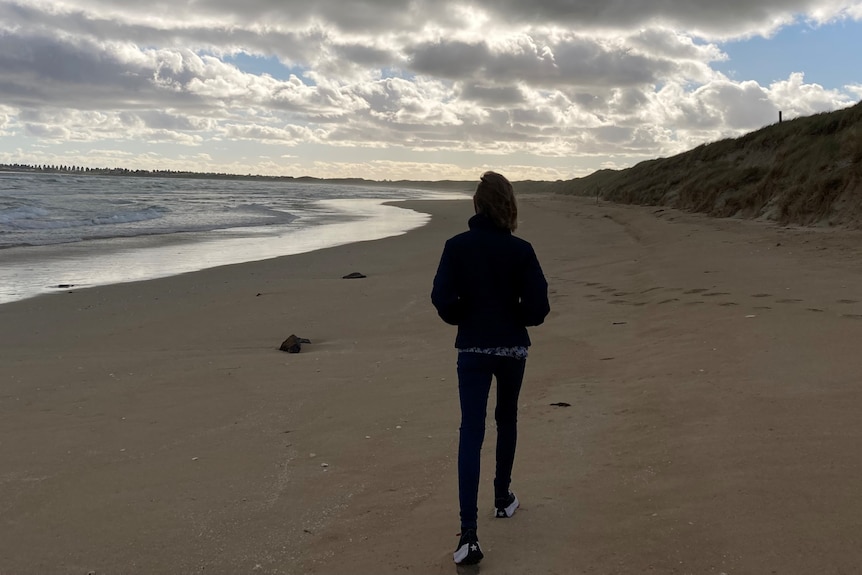 A teen boy walks along a beach.