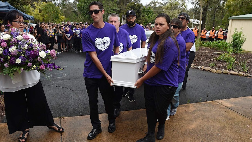 Pallbearers dressed in purple T-shirts carry a white coffin into a funeral service