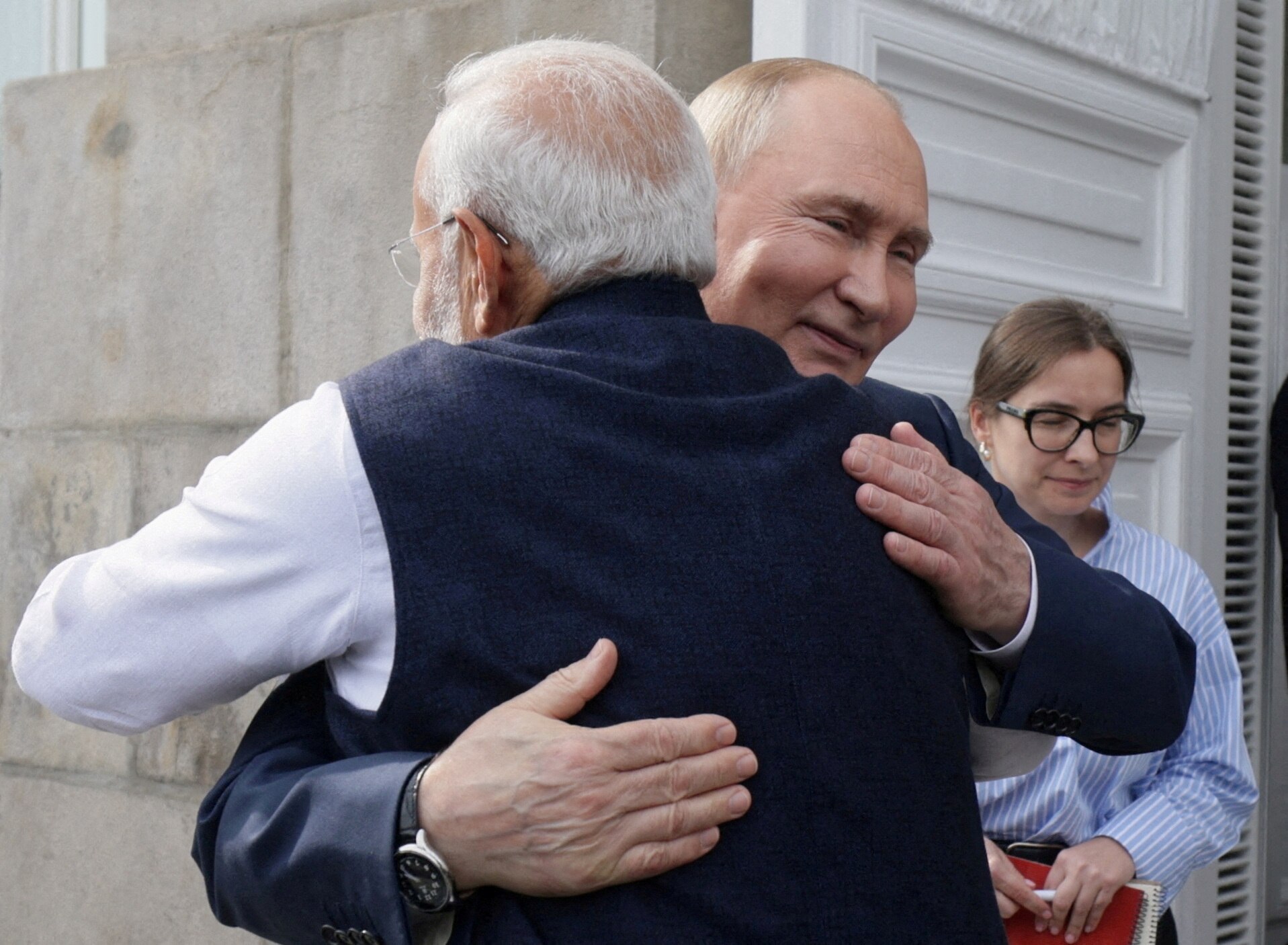 A smiling Putin hugs Modi while wearing a suit outside in a close up image
