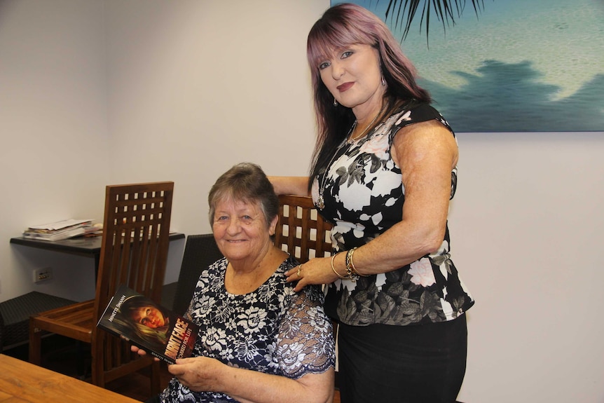 One woman sits and one stands at a table