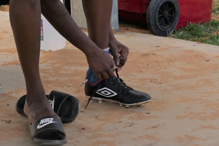 A woman laces up her football boots in Barunga