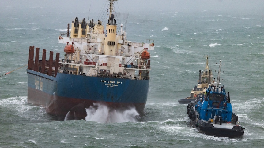 A bulk carrier and two tug boats thrash around in big swell