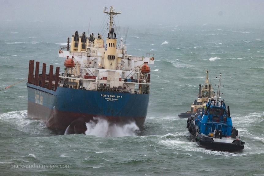 A bulk carrier and two tug boats thrash around in big swell