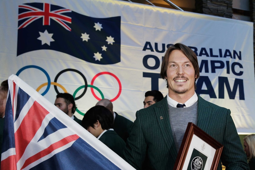A man holds an Australian flag in front of the Olympic rings