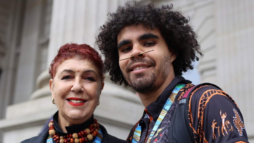 Carolyn Briggs and Jordan Edwards stand side-by-side smiling on the steps of Victorian Parliament.