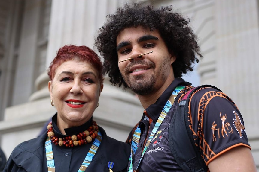 Carolyn Briggs and Jordan Edwards stand side-by-side smiling on the steps of Victorian Parliament.