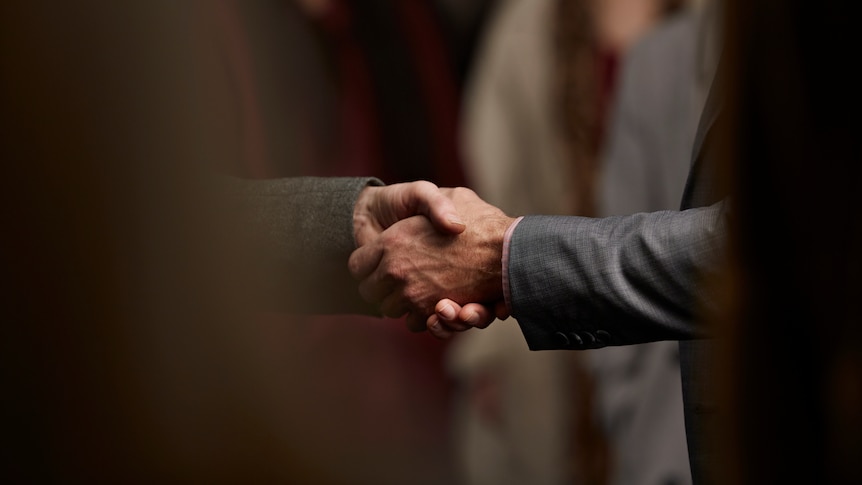  A shadowy close up of a handshake between two men in suits