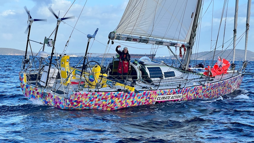 Lisa stands waving from her boat in the ocean