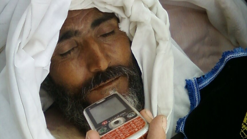A dead man with someone holding a phone close to him.