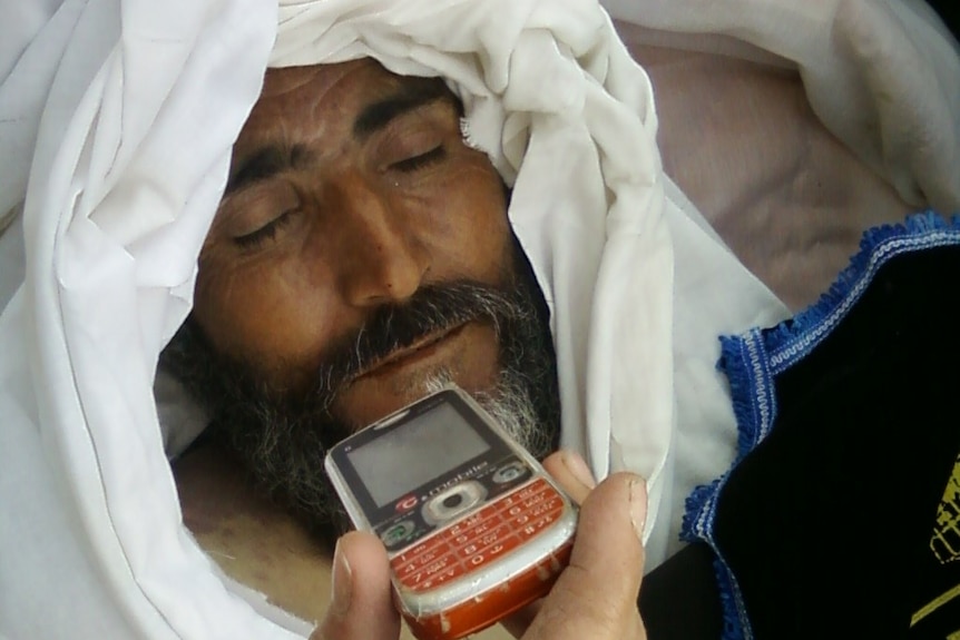 A dead man with someone holding a phone close to him.