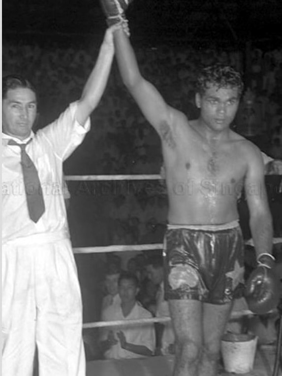 A black and white image of a young boxer with his arm in the air, next to a trainer.