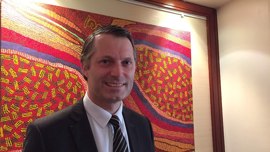 Man in suit pictured in front of unrelated Aboriginal dot painting.