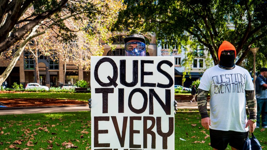 A man holds a sign that says 'question everything'