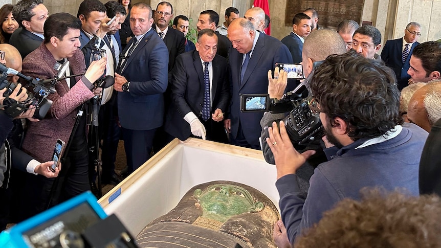 Egyptian officials talk in front of an ancient wooden sarcophagus during a handover ceremony.